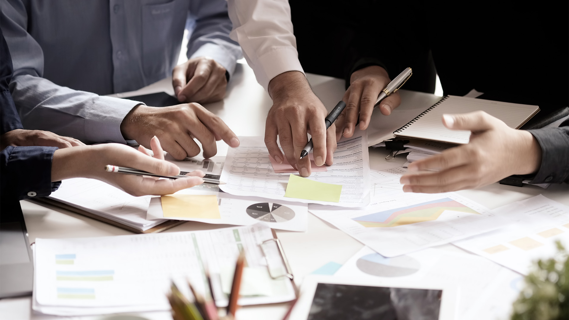 Hands crowded around paper on a desk. People making a decision.